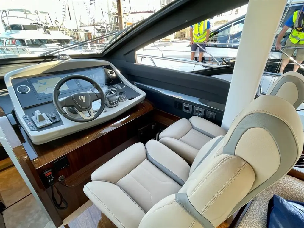 Interior view of a yacht's modern control panel, featuring a steering wheel, touchscreen displays, and comfortable seating.